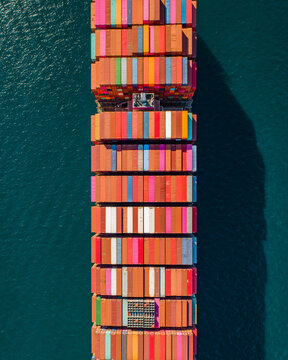 Aerial view of the Port of Long Beach showing a large container ship loaded with colorful shipping containers floating on deep blue water in Long Beach, California, United States.