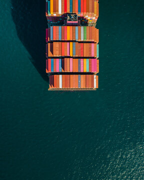 Aerial view of a large container ship loaded with colorful shipping containers navigating the deep blue waters of the Port of Long Beach, Long Beach, California, United States.