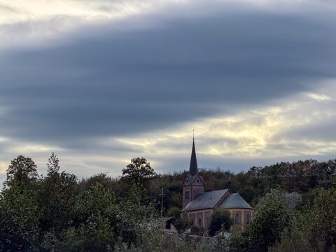 Reuland, Belgium, September 11, 2026 - Historic Church Steeple Rising Above Treetops Under Dramatic Storm Clouds in Reuland, Belgium