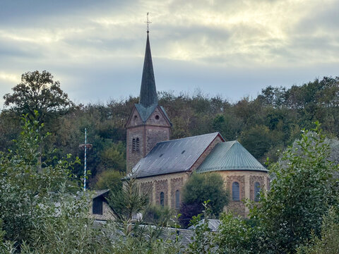 Reuland, Belgium, September 11, 2026 - Historic Romanesque Stone Church with Tall Spire in Reuland, Belgium, Surrounded by Autumn Trees