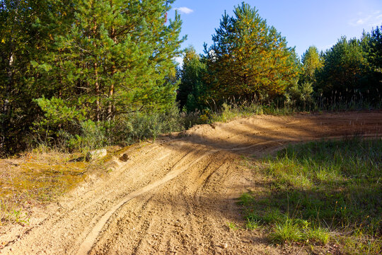Sandy enduro track winding through a pine forest, featuring deep tire ruts from off-road motorcycle training in a former quarry, captured on a bright sunny day