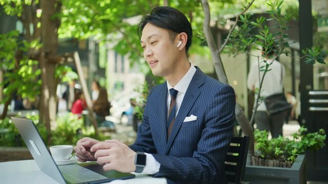 Japanese businessman smiling in a remote meeting at a cafe terrace