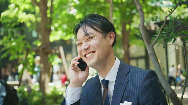 Japanese businessman laughing on the phone at a cafe terrace