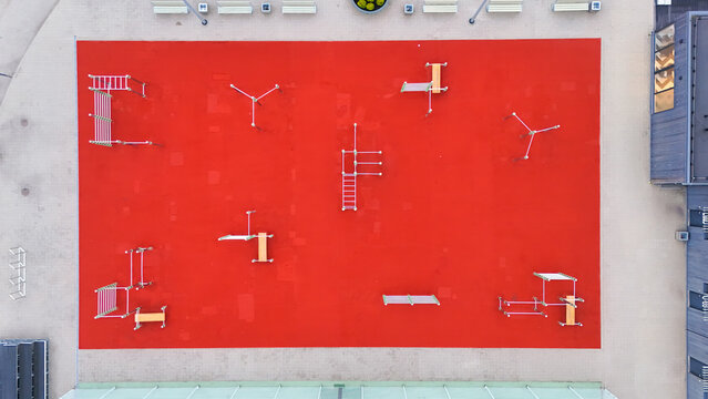Aerial view of a modern playground with a vibrant red rubber surface, featuring various climbing frames and exercise equipment in Riga, Latvia.