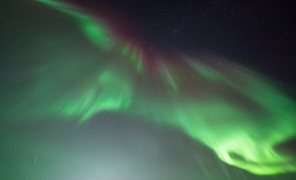 View of vibrant green and red aurora borealis dancing across the dark night sky in the arctic wilderness Norway.