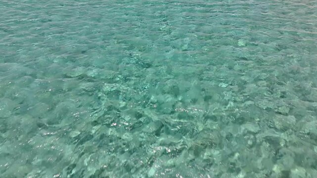 Clear turquoise water ripples above the visible seabed at Paralia Firiplaka on Milos, Greece, as sunlight forms shifting bright patterns across submerged rocks and sand.