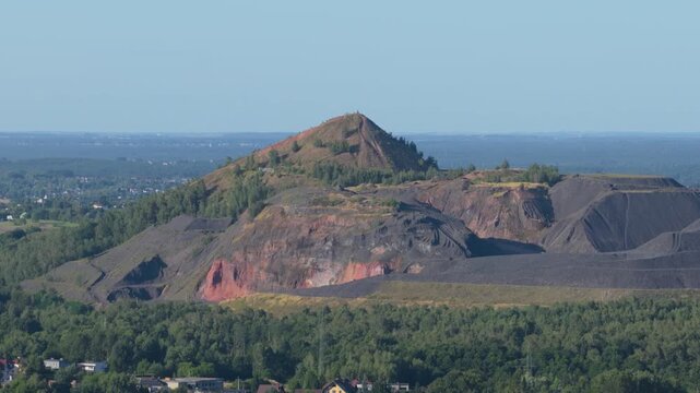 Aerial view of a large coal mine spoil tip surrounded by lush green forest