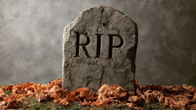 Close up of old weathered gravestone with RIP inscription surrounded by dried autumn leaf on ground against grey wall