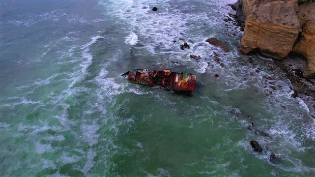 Aerial orbit around VICMAR shipwreck as waves break over shallow water and rocks along the rugged Baja California coast, Mexico
