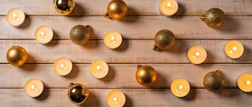 overhead flat lay view of golden christmas baubles and burning tealight candles arranged on rustic white wooden background forming seasonal holiday celebration border design pattern