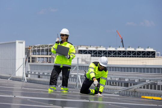 Solar engineers team in safety vests and hard hats working on rooftop solar panels project, Workers collaborating on solar power plant installation and maintenance roof project
