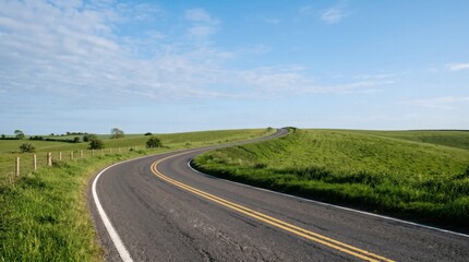 Fototapeta premium Curving asphalt road through green rolling hills under a blue sky with clouds.