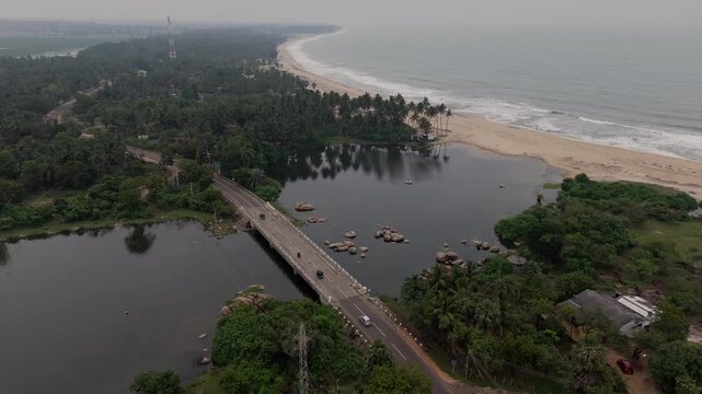 Cinematic aerial static drone shot of a bridge with a tuk tuk and traffic crossing a crocodile infested river in Komari near Pottuvil on the tropical east coast of Sri Lanka