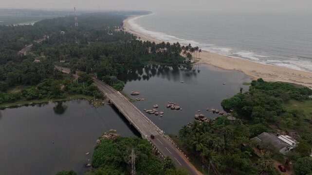 Cinematic aerial drone tracking shot following a tuk tuk driving across a bridge over a crocodile infested river in Komari Sri Lanka with the ocean in the background