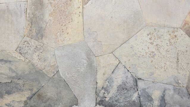 Natural stone wall texture with orange and grey stones. Vintage rustic stone wall background with dark stains. Close-up of a rustic stone cladding wall showing organic polygonal shapes.