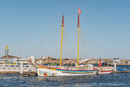 View of a colorful traditional Portuguese fishing boat docked in the marina with bright floral patterns on its hull under a clear blue sky in Lagos, Faro District, Portugal.