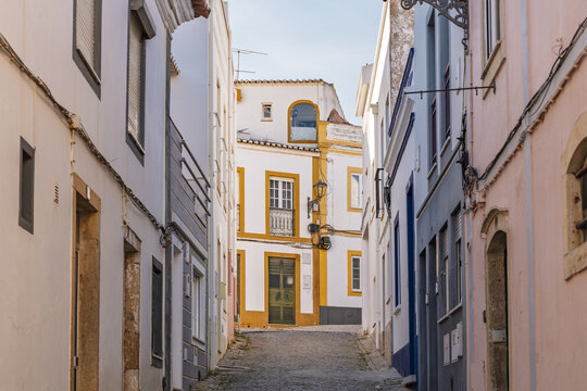 View of a narrow cobblestone street in the historic old town of Lagos, lined with traditional Portuguese buildings featuring colorful facades and yellow trim in Lagos, Faro District, Portugal.
