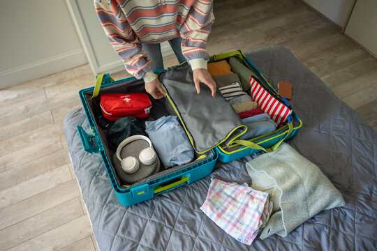 Luggage organization and packing for solo trip, woman packs clothing and personal items in suitcase, smart and stress-free preparations for journey, female neatly placing things inside travel case.