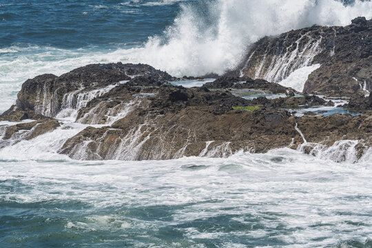 View of powerful Atlantic waves crashing against the dark rocky coastline and natural tide pools in Sines, Setubal, Portugal.