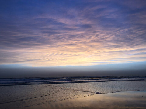 Blue twilight over the ocean with a curving wave line on the beach, Costa da Caparica, Portugal