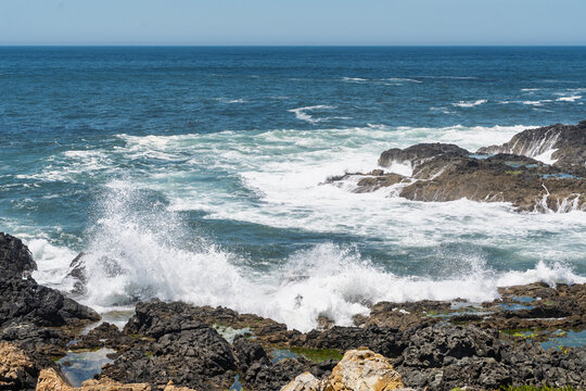 View of waves crashing against dark, jagged volcanic rocks on the coast of Sines, Setubal, Portugal.