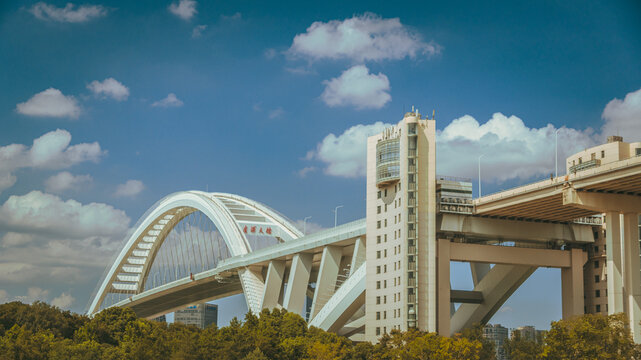 View of Lupu Bridge with its iconic steel arch structure and concrete support pillars under a bright blue sky with scattered clouds Shanghai, China.