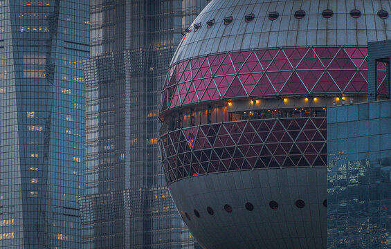 View of the spherical structure of the Oriental Pearl Tower with its pink lattice design, set against the reflective glass facades of modern skyscrapers in Lujiazui, Shanghai, China.