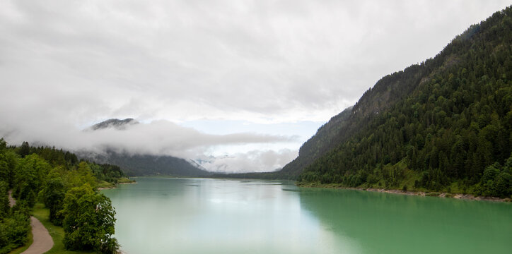 View of the turquoise waters of the lake surrounded by dense pine forests and misty mountains in Eng, Tyrol, Austria.