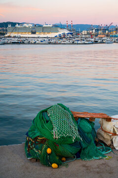 View of fishing nets piled on the dock with a cruise ship and boats in the harbor at sunset in La Spezia, Liguria, Italy.