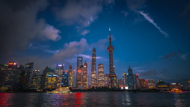 View of the illuminated Lujiazui skyline featuring the Oriental Pearl Tower and modern skyscrapers reflecting over the Huangpu River at dusk in Shanghai, China.