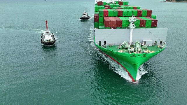 green container ship fully loaded with colorful cargo escorted by two tugboats in the sea. Global maritime logistics, international shipping trade, and freight transport.