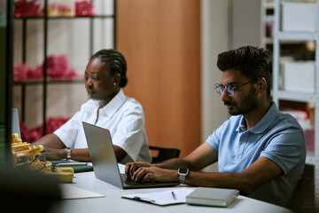 Fototapeta premium Young Indian man and African American woman programming robotics hardware on laptops in tech laboratory. Commercial image ideal for engineering education and STEM technology marketing