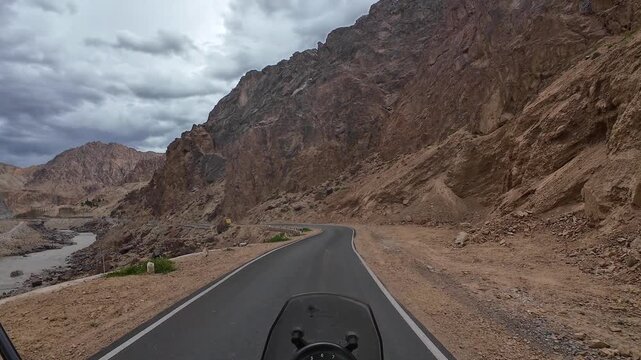 Dah Hanu valley, India : Point of view footage of motorcycle rides on narrow road by river in Aryan valley or Dah Hanu valley in Ladakh, India surrounded by arid mountain under dramatic cloudy sky