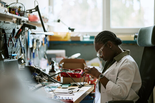 African American young female engineer assembling electronic wires at laboratory workbench. Useful for STEM education campaigns and technology innovation marketing