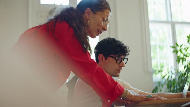 Woman works with a younger man at the computer during mentoring and teamwork, highlighting coaching, workplace learning, communication, and problem solving in an office setting.