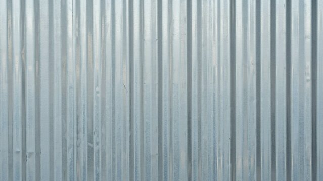 Corrugated metal texture with vertical ridges, silver galvanized steel sheet background, industrial metallic surface for construction and architectural design concepts.