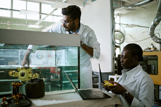 Young Indian man and African American woman testing underwater robot in water tank using controller and laptop. Scene suitable for marine robotics engineering research promotion