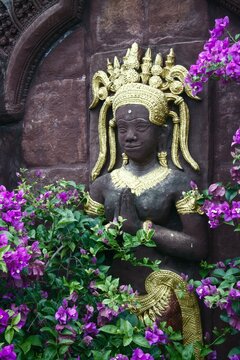 Ancient Angkor style stone apsara statue adorned with vibrant pink bougainvillea in resort garden