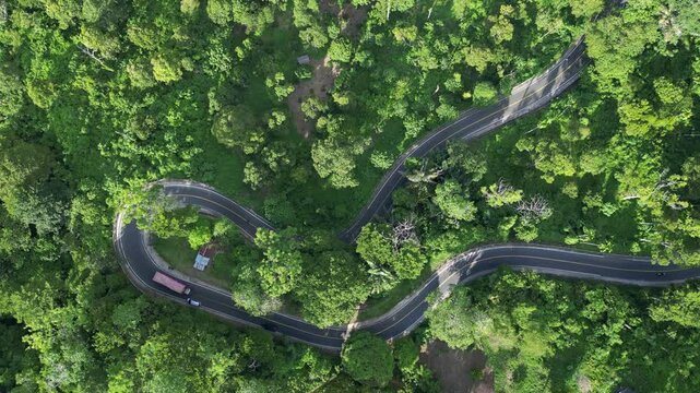 Banda Aceh, Indonesia : Top down and rotating aerial drone footage of cars drive on the winding mountain road surrounded by rain forest near Banda Aceh of Sumatera, Indonesia
