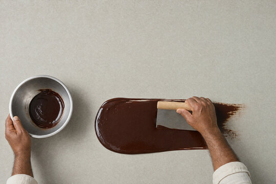 Chocolatier hand tempering dark chocolate on a stone slab overhead