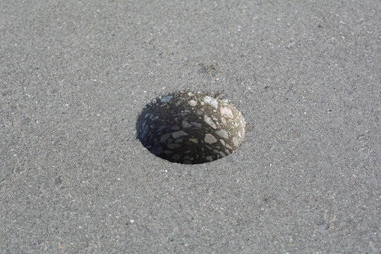 Single circular core hole in gray concrete pavement exposes aggregate structure during road inspection, testing and repair work.