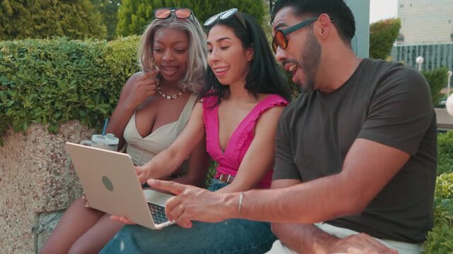 Diverse friends discussing project on laptop in city park