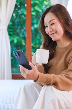 Vertical portrait image of a woman holding and using smart phone on the bed at home