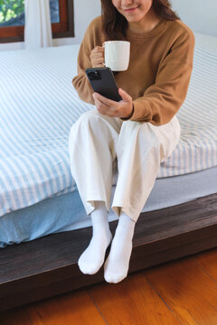 Vertical closeup image of a woman holding and using smart phone on the bed at home