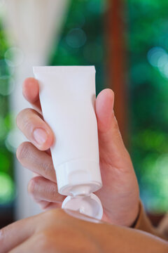 Vertical closeup image of a woman holding a white tube and applying cream on hand