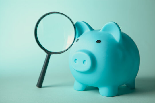 Piggy bank and magnifying glass on blue background,