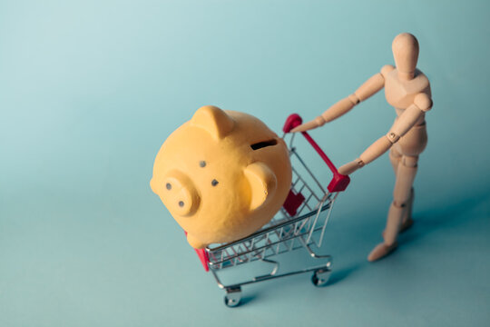 Piggy bank in shopping cart on blue background. Concept of saving money.
