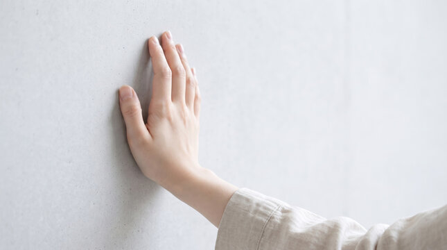 コンクリート壁に手を触れて感触を確かめる女性の手元