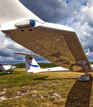 White glider wing showing landing gear details and a rudder with a german flag, parked on a summer airfield