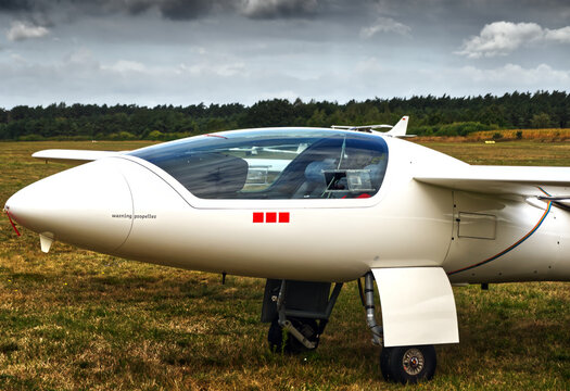 White motor glider on a grassy airfield, parked with landing gear extended, waiting for flight or maintenance